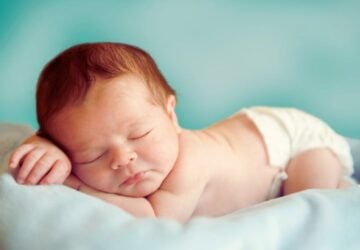 Newborn baby lying on a blanket. Has a nappy on.
