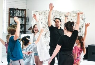 Backbone Youth Arts Young Creators Camp drama students with arms in the air with instructor.