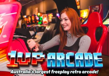 1UP Arcade girl sitting at retro arcade driving game.