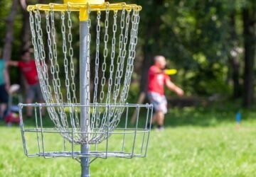 A player throwing a disc toward the disc golf basket.