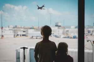 Two young children looking out the window at a plane leaving the airport.