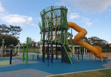 Large green and yellow play tower with yellow tunnel slide at North Lakes Town Park at Lake Eden.