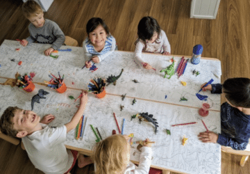 Small Scholars group of kindergarteners around table drawing with dinosaurs.